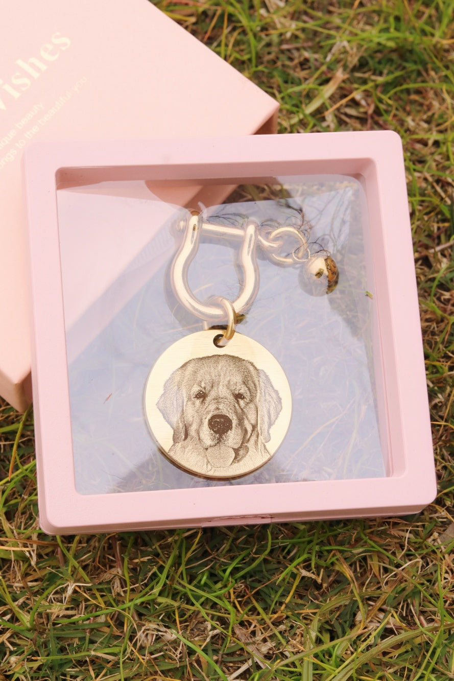 Gold keychain with engraved dog's face in a pink box on grass