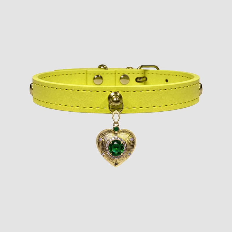 Yellow leather choker with a heart-shaped charm featuring a green gemstone on a light gray background