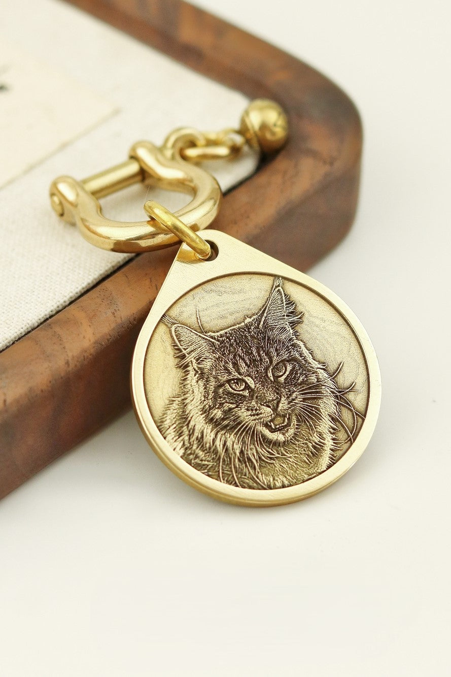 Gold keychain with a cat's face engraving on a wooden surface