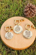 Three gold dog tags with engraved pet names on a wooden stand outdoors.