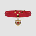 Red leather choker with a gold heart-shaped pendant featuring a red gemstone on a light gray background.