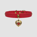 Red leather choker with a gold heart-shaped pendant featuring a red gemstone on a light gray background.