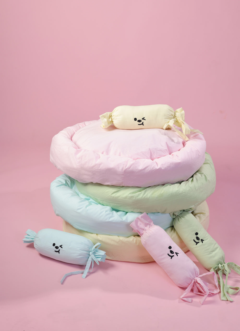 Stack of pastel-colored cushions with decorative elements on a pink background