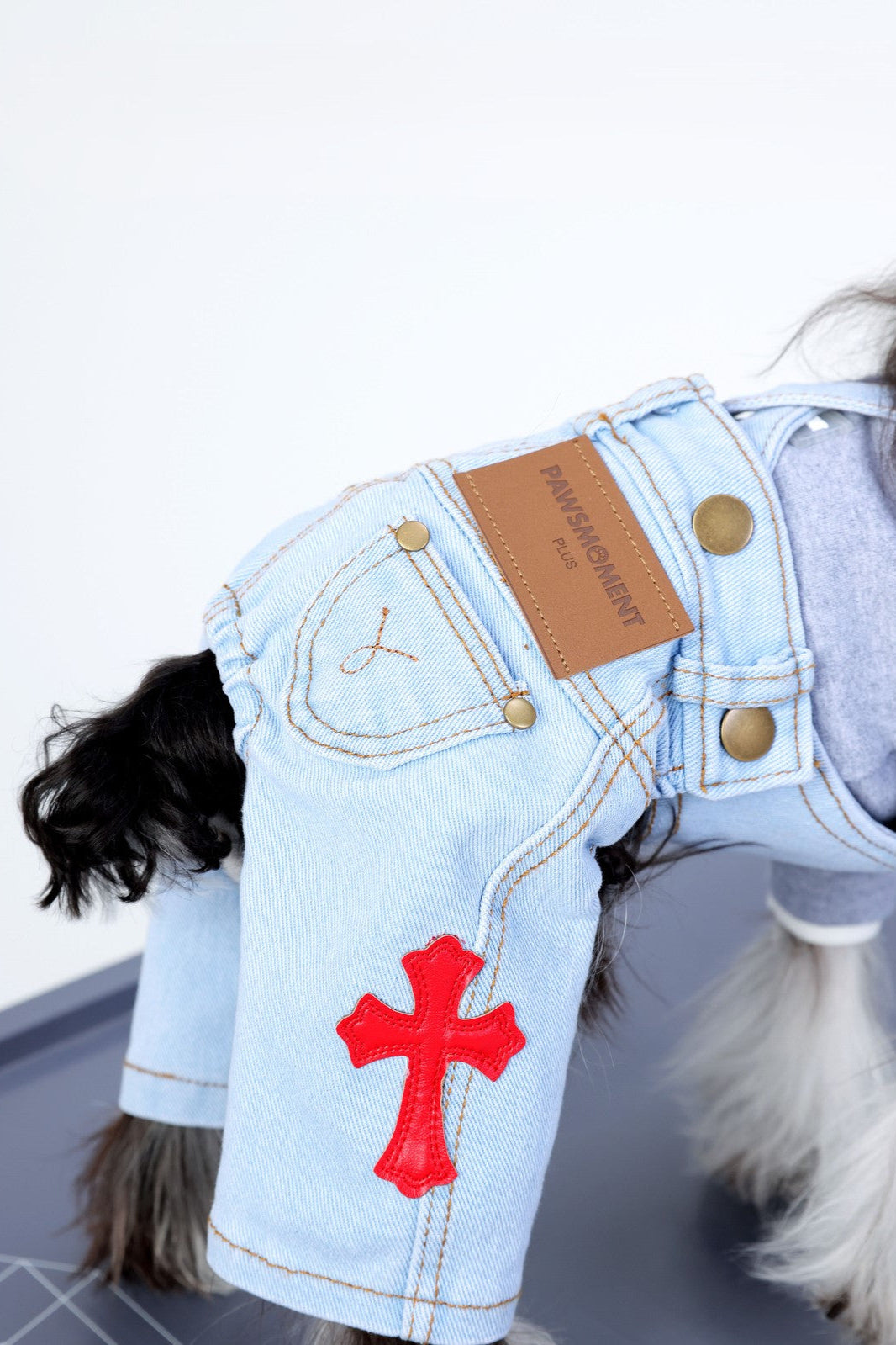 Dog wearing a denim outfit with a red cross patch on a white background